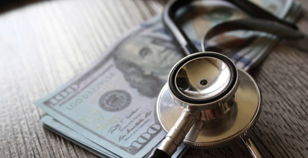 FEHB, OPM, GAO costs, Stethoscope and money on wooden table representing health care, FEHB plans.